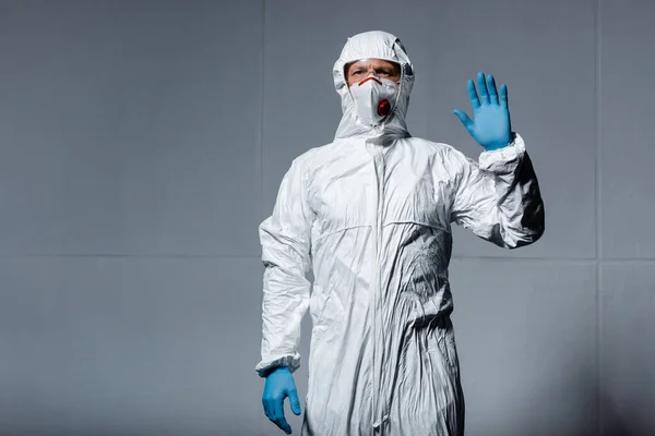 Uomo in dispositivi di protezione individuale agitando mano su grigio — Foto stock