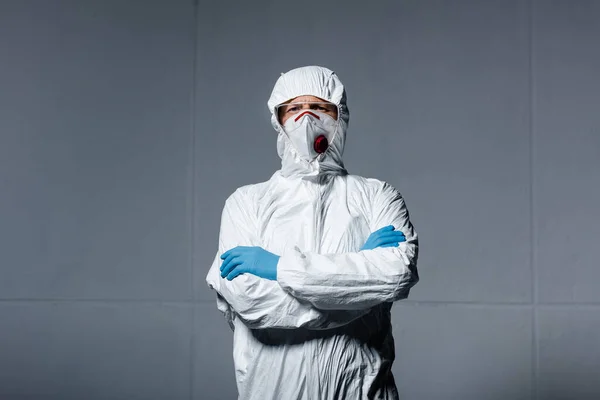 Hombre en equipo de protección personal de pie con los brazos cruzados en gris - foto de stock