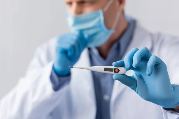 Selective focus of mature doctor in latex gloves holding digital thermometer and coughing isolated on grey — Stock Photo