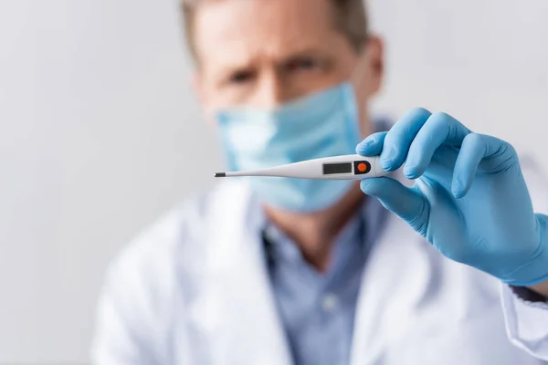 Selective focus of mature doctor in latex glove holding digital thermometer isolated on grey — Stock Photo