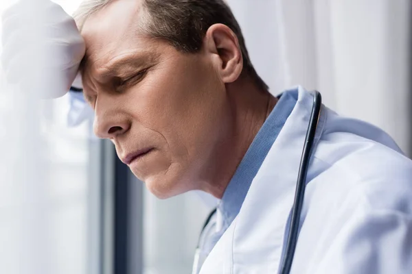 Втомлений лікар середнього віку з закритими очима біля вікна в клініці — стокове фото