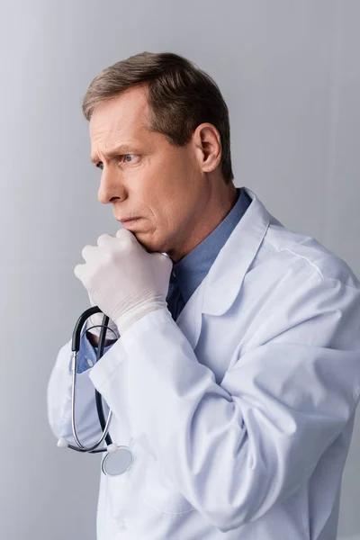 Nachdenklicher und reifer Arzt in weißem Mantel auf grau — Stockfoto