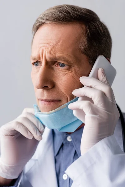Stressed middle aged doctor talking on smartphone isolated on grey — Stock Photo