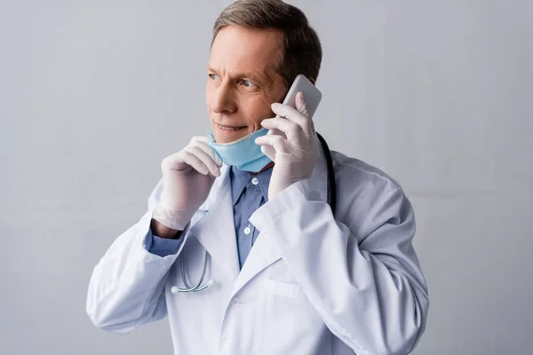 Happy middle aged doctor talking on smartphone on grey — Stock Photo