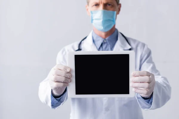 Enfoque selectivo de médico maduro en máscara médica celebración tableta digital con pantalla en blanco aislado en blanco - foto de stock