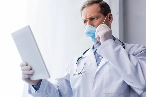 Вибірковий фокус зрілого лікаря в медичній масці з використанням цифрового планшета на білому — стокове фото