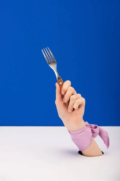 Cropped view of woman with ribbon on hand holding fork isolated on blue — Stock Photo