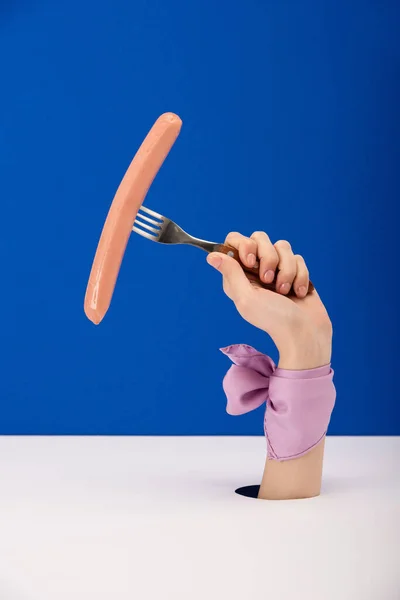 Cropped view of woman with ribbon on hand holding fork with tasty sausage isolated on blue — Stock Photo