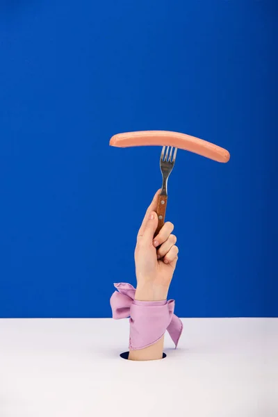 Vista ritagliata di donna con nastro sulla forchetta tenuta in mano con salsiccia isolata su blu — Foto stock