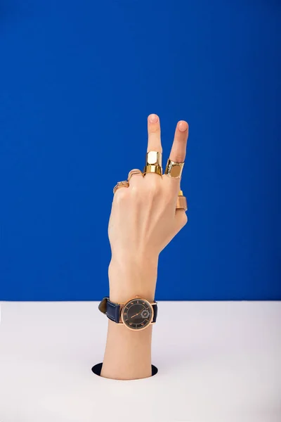 Cropped view of woman with wristwatch and rings showing peace sign isolated on blue — Stock Photo