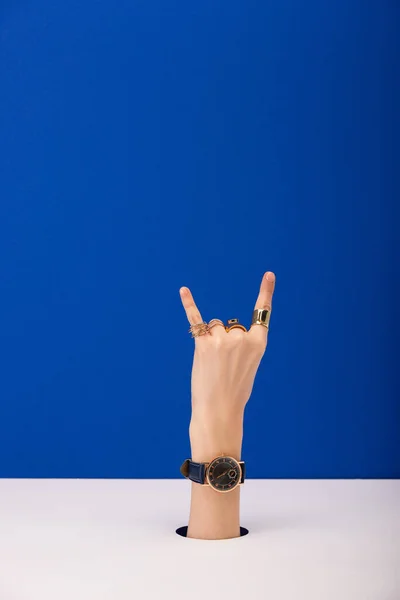 Vista cortada de mulher com relógio de pulso na mão mostrando sinal de rocha isolado no azul — Fotografia de Stock