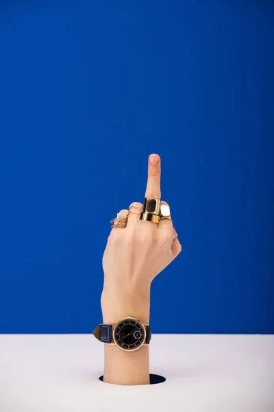 Vista recortada de la mujer con reloj de pulsera en la mano que muestra el dedo medio aislado en azul - foto de stock