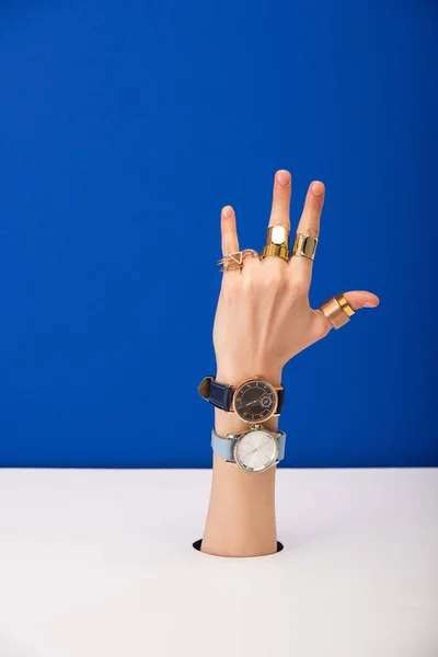 Vista recortada de la mujer con relojes de pulsera en la mano y anillos de oro aislados en azul - foto de stock
