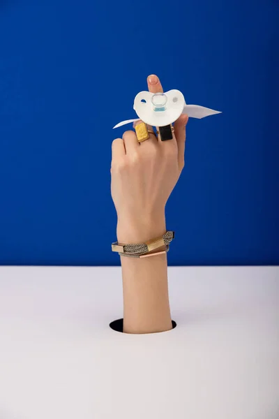 Vista ritagliata di donna con braccialetto e anelli d'oro con ciuccio in silicone isolato su blu — Foto stock