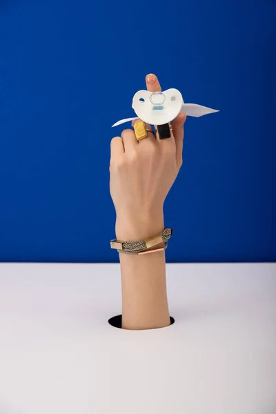 Cropped view of woman with bracelet and golden rings holding silicone pacifier isolated on blue — Stock Photo