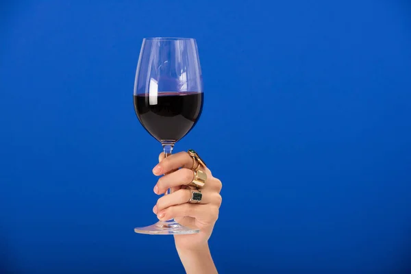 Vue recadrée de la femme avec des anneaux sur les doigts tenant verre avec du vin rouge sur bleu — Photo de stock