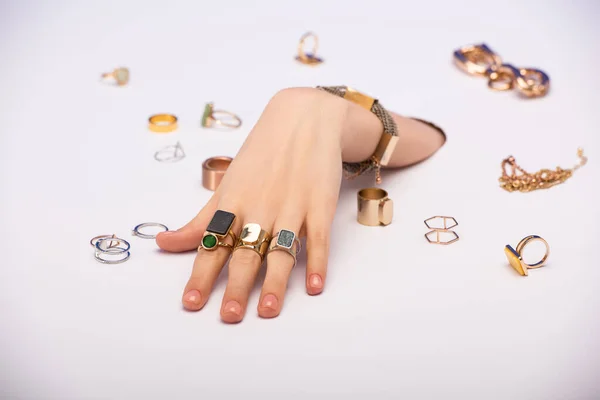 Cropped view of woman with bracelet on hand near golden rings on white — Stock Photo