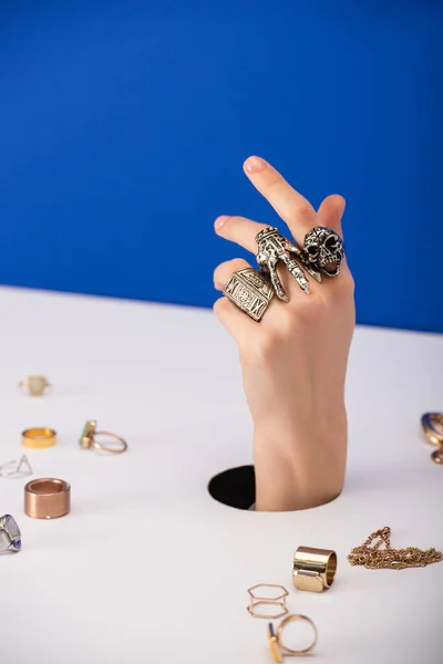 Enfoque selectivo de la mujer con brazalete en la mano cerca de anillos de oro aislados en azul - foto de stock