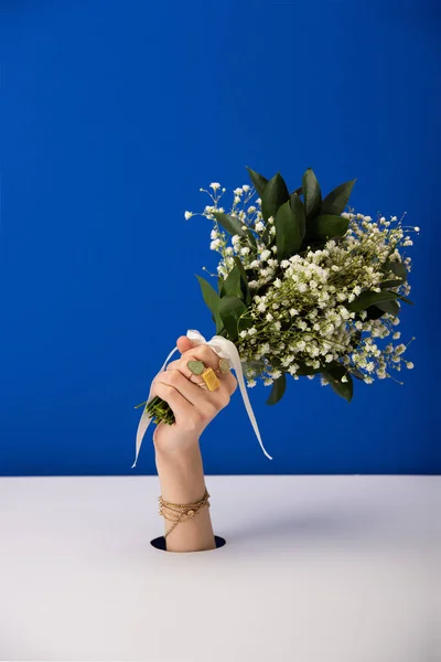 Vista ritagliata della donna con braccialetto che tiene bouquet di piccoli fiori primaverili isolati su blu — Foto stock