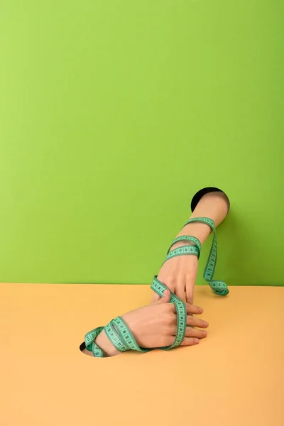 Cropped view of woman with measuring tape on hands on green and orange — Stock Photo