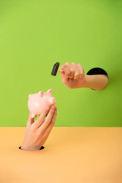 Cropped view of woman holding small hammer and pink piggy bank on green and orange — Stock Photo