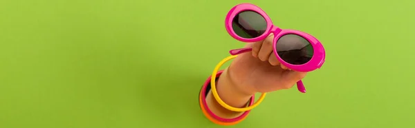 Panoramic shot of woman holding pink sunglasses on green — Stock Photo