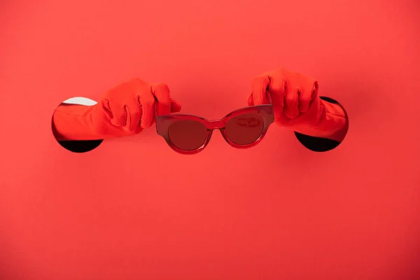 Обрезанный вид женщины в перчатках с модными солнцезащитными очками на красном — стоковое фото