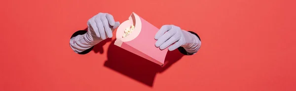 Panorama-Aufnahme einer Frau in Handschuhen, die einen Popcorn-Eimer auf Rot hält — Stockfoto
