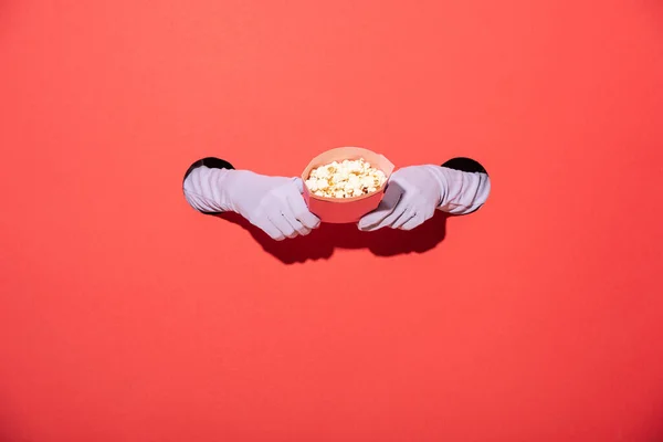 Vista ritagliata della donna in guanti che tengono secchio con gustosi popcorn sul rosso — Foto stock