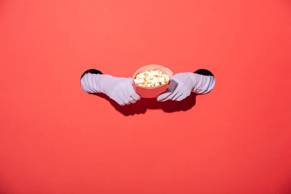 Vista recortada de la mujer en guantes sosteniendo cubo con sabrosas palomitas de maíz en rojo - foto de stock