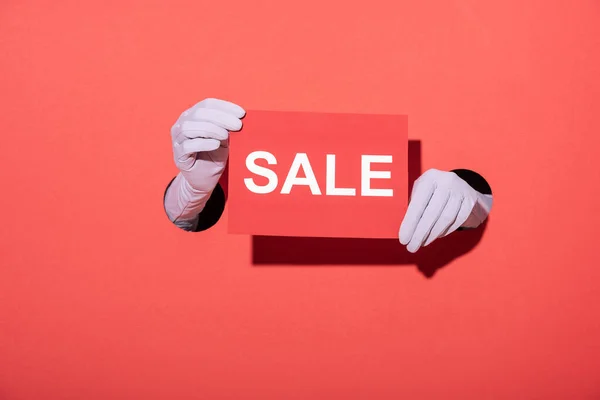 Cropped view of woman in gloves holding paper with sale lettering on red — Stock Photo