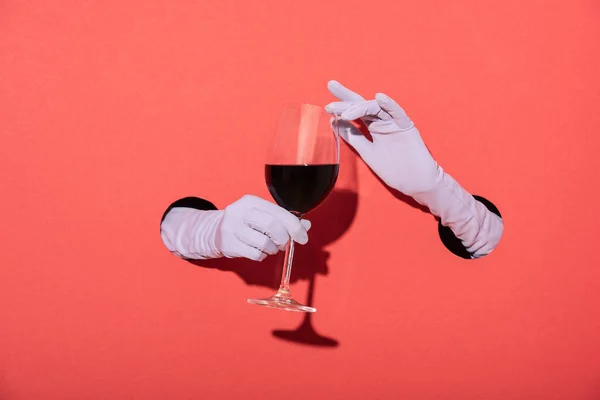 Cropped view of woman in gloves holding glass with red wine on red — Stock Photo