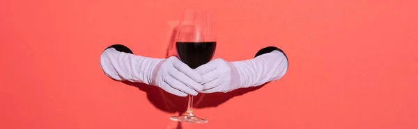 Prise de vue panoramique de la femme dans des gants tenant verre avec du vin rouge sur rouge — Photo de stock