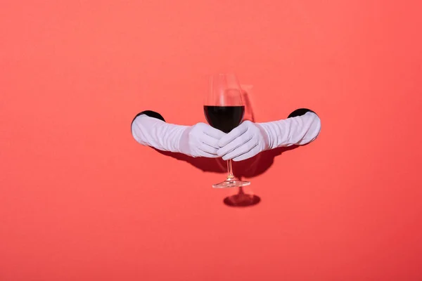 Cropped view of woman in gloves holding glass of red wine on red — Stock Photo