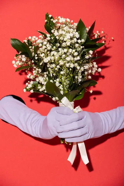 Vue recadrée de la femme en gants tenant bouquet de fleurs blanches de printemps sur rouge — Photo de stock