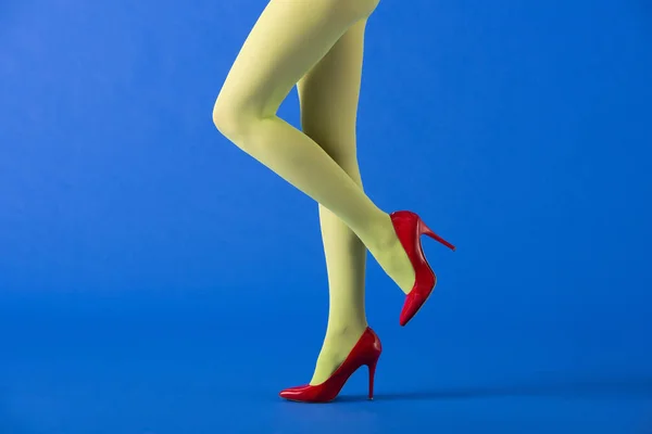 Vista recortada de modelo en medias verdes y tacones rojos posando en azul - foto de stock