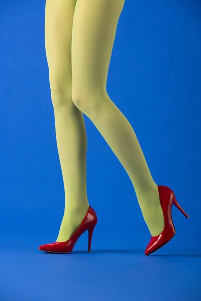 Vista cortada do modelo na moda em meias verdes e saltos vermelhos posando em azul — Fotografia de Stock
