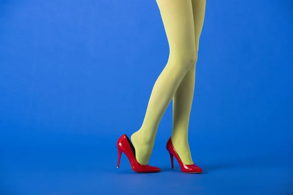 Vista recortada de modelo elegante en medias verdes y tacones rojos posando en azul - foto de stock