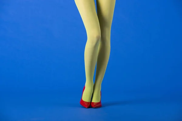 Ausgeschnittene Ansicht des Models in grünen Strumpfhosen und High Heels, die auf blau posieren — Stockfoto