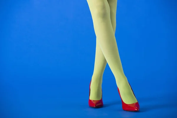 Vista recortada de la mujer en medias verdes y tacones rojos posando en azul - foto de stock