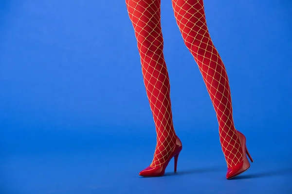 Vista ritagliata della donna in calze a rete e tacchi rossi in posa su blu — Foto stock