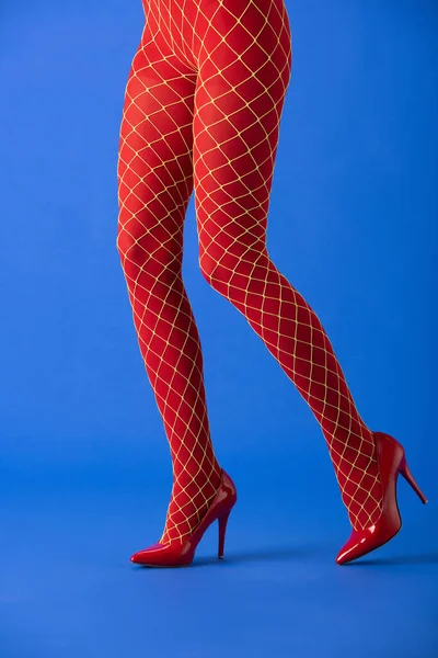Vista recortada del modelo en medias de rejilla y tacones rojos posando en azul - foto de stock