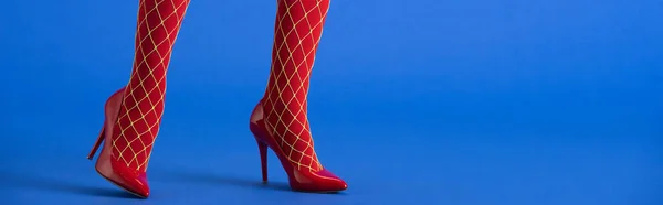 Colpo panoramico di donna in calze a rete e tacchi rossi in posa su blu — Foto stock