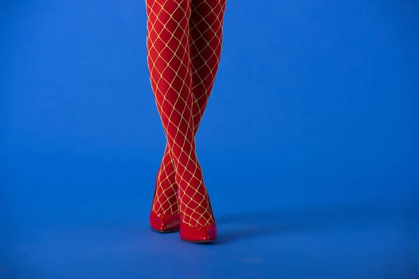 Vue recadrée de la femme en rouge collants résille et talons debout sur bleu — Photo de stock