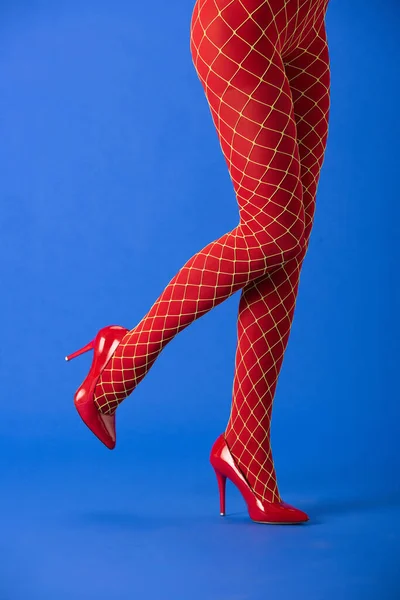 Ausgeschnittene Ansicht einer Frau in roten Netzstrumpfhosen und High Heels, die auf blau posiert — Stockfoto