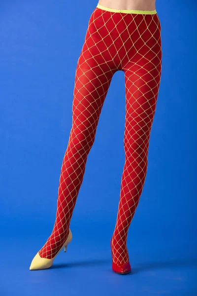 Vista ritagliata del modello in calze a rete, tacchi gialli e rossi in piedi su blu — Foto stock