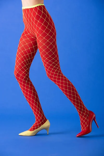 Cropped view of woman in fishnet tights, yellow and red heels posing on blue — Stock Photo