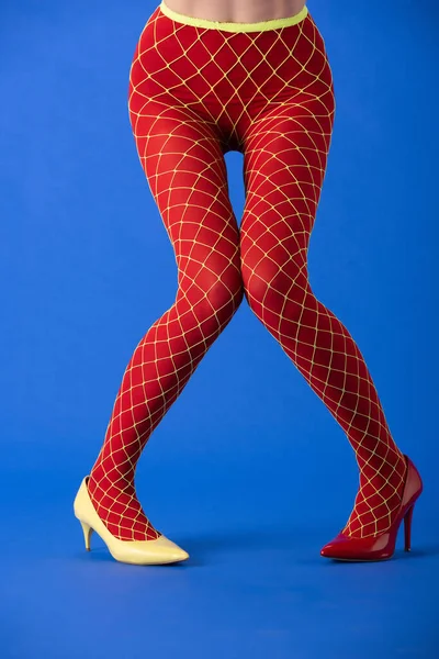 Cropped view of model in fishnet tights, yellow and red heels on blue — Stock Photo
