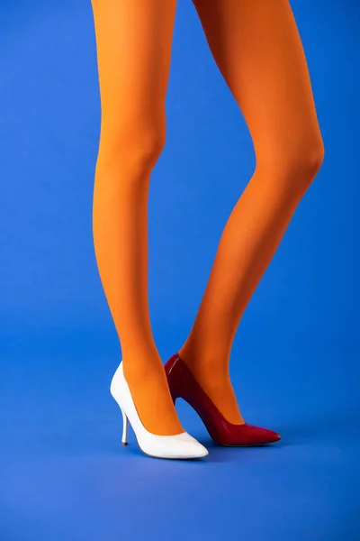 Vista cortada do modelo na moda em meias brilhantes, saltos brancos e vermelhos posando em azul — Fotografia de Stock