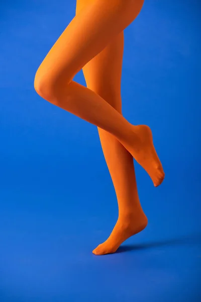 Cropped view of woman in bright orange tights posing on blue — Stock Photo